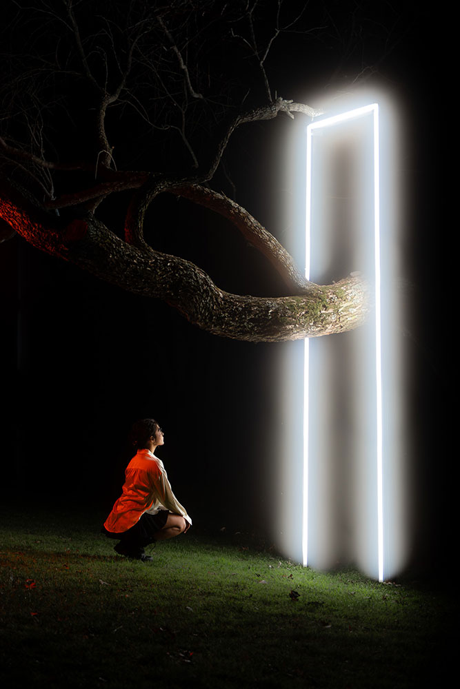 Arturo Carillo photo of a woman in a red blouse at night looking at a white shining door frame around a tree limb