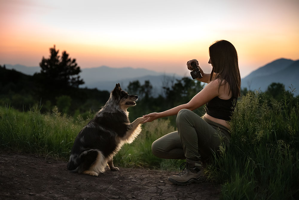 photo of Madi Clark photographing her dog, while holding her paw, at sunset