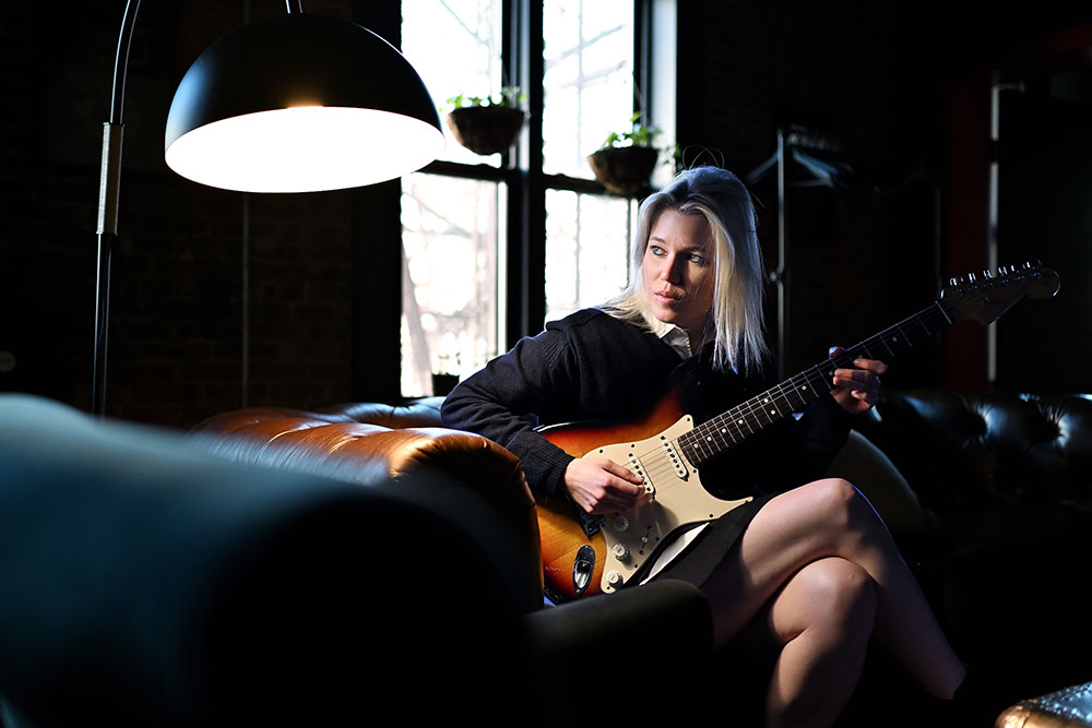 Todd Owyoung photo of a female guitarist holidng her guitar backstage lit by one light